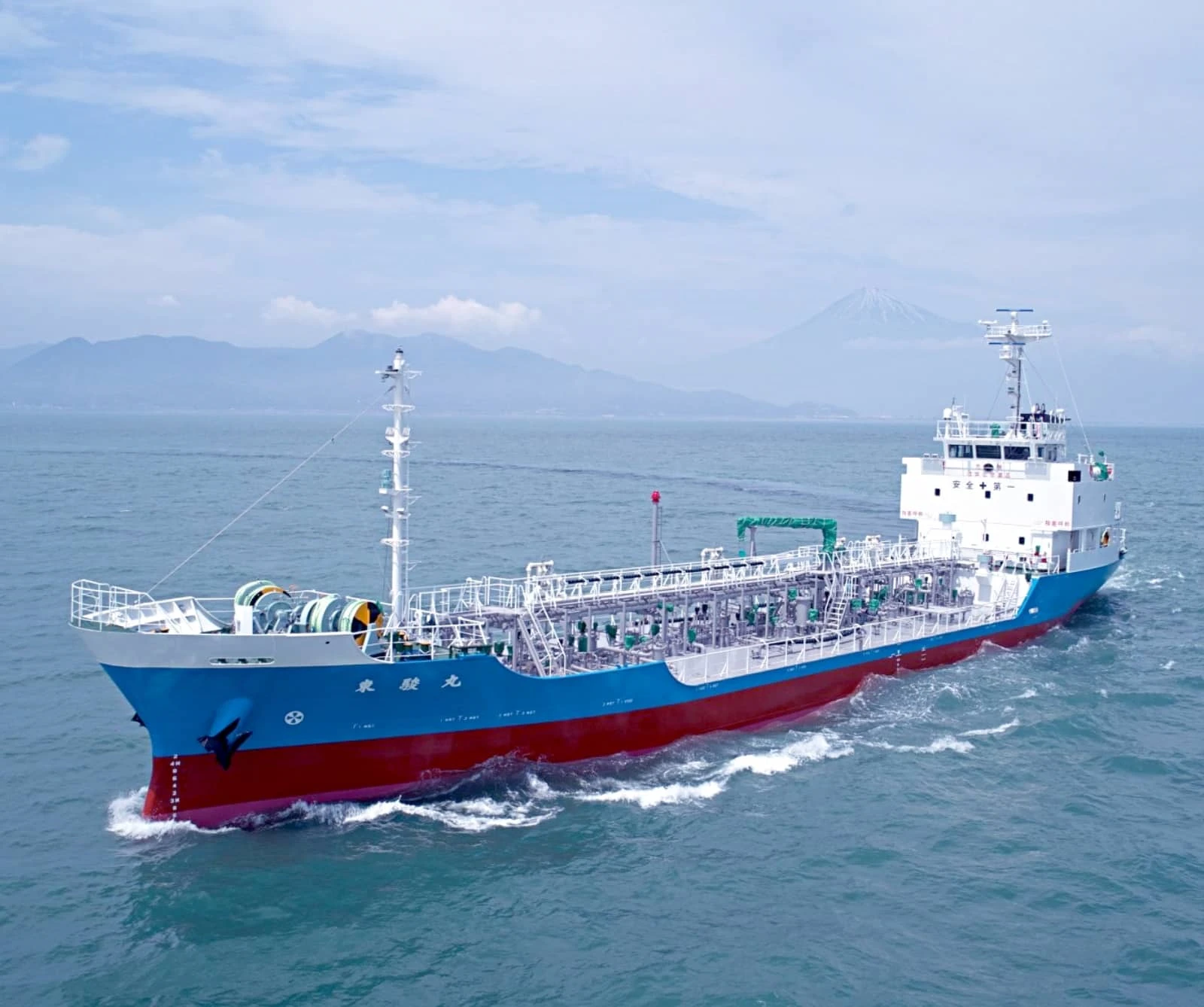 富士山を背景に海を進む青と赤の船体の貨物船