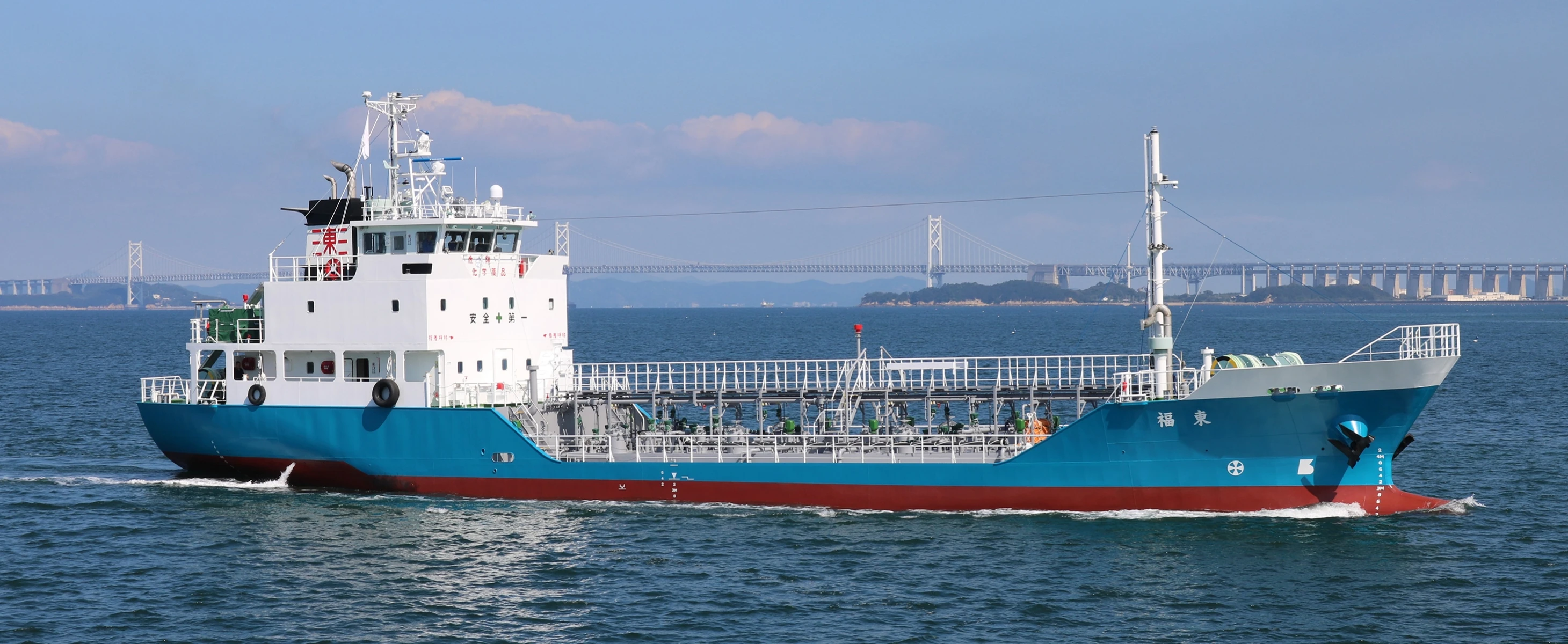 巨大な橋を背景に海を進む内航タンカー。青い船体と白いブリッジが特徴