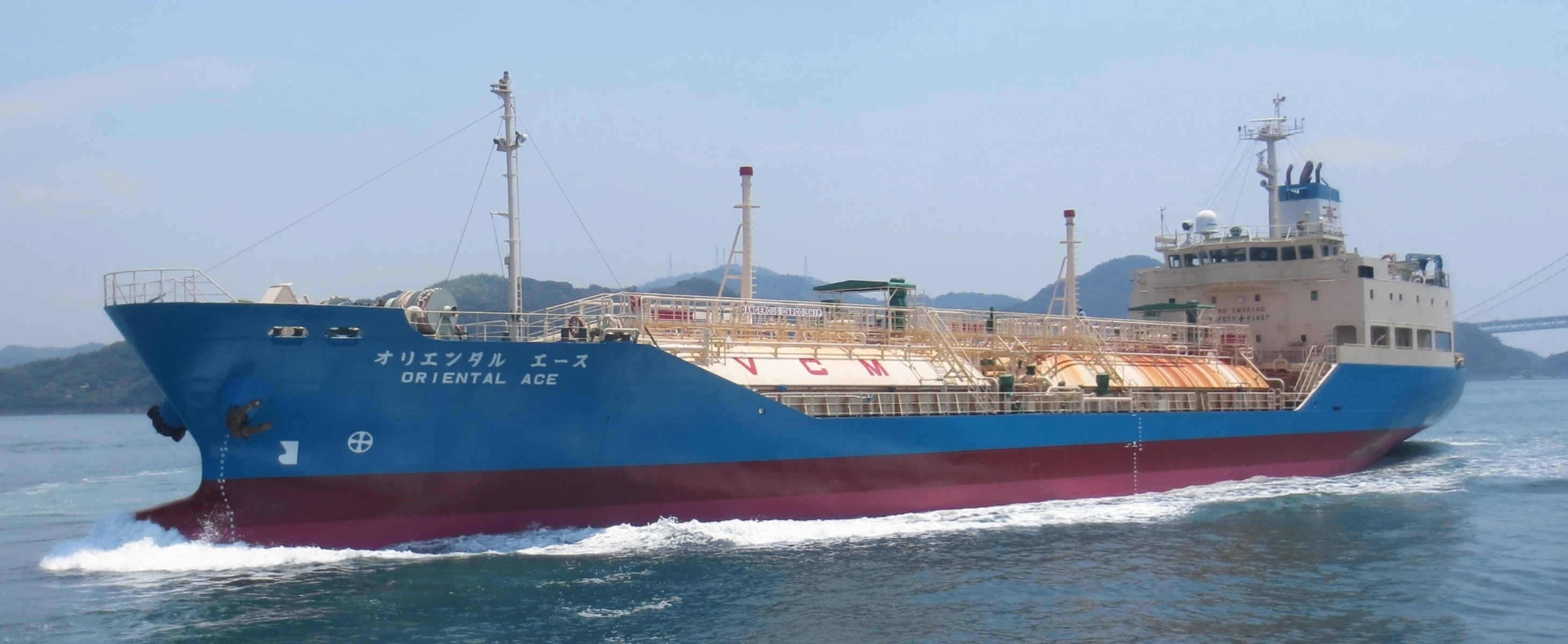 航行中の液化ガスキャリアの外観。背景に山並みと橋