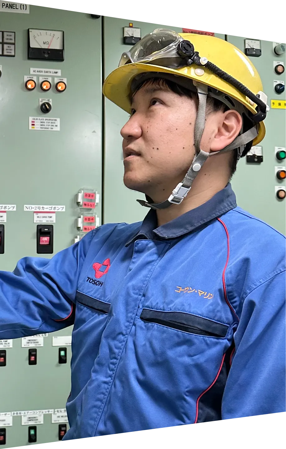 制御パネルの前で点検作業を行う、ヘルメットを被った若い船員