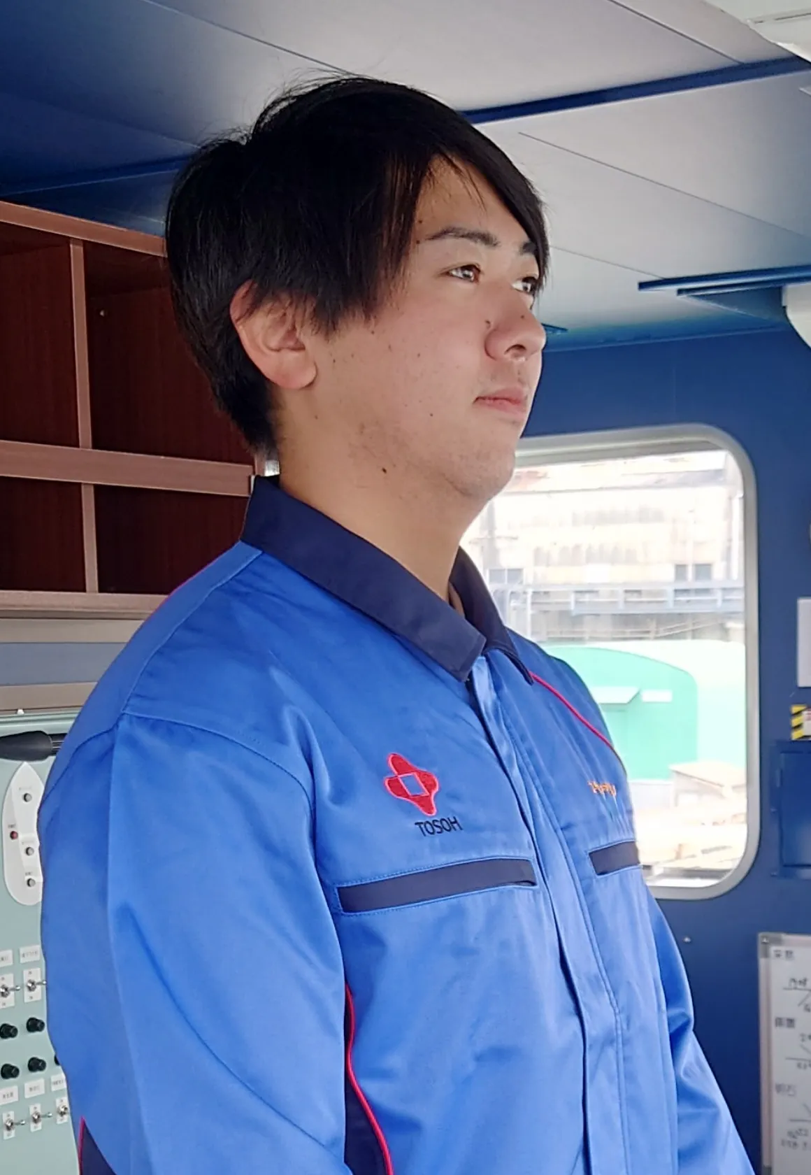 船橋（ブリッジ）で前方を注視する青い作業着の若手船員