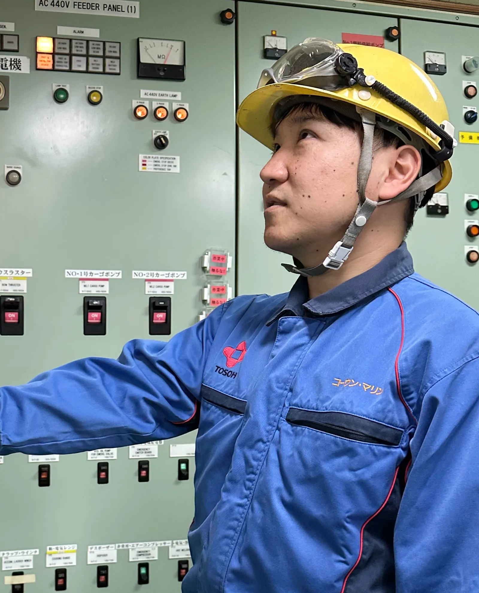 制御パネルの前で点検作業を行う、ヘルメットを被った若い船員