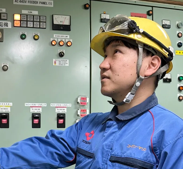 制御パネルの前で点検作業を行う、ヘルメットを被った若い船員