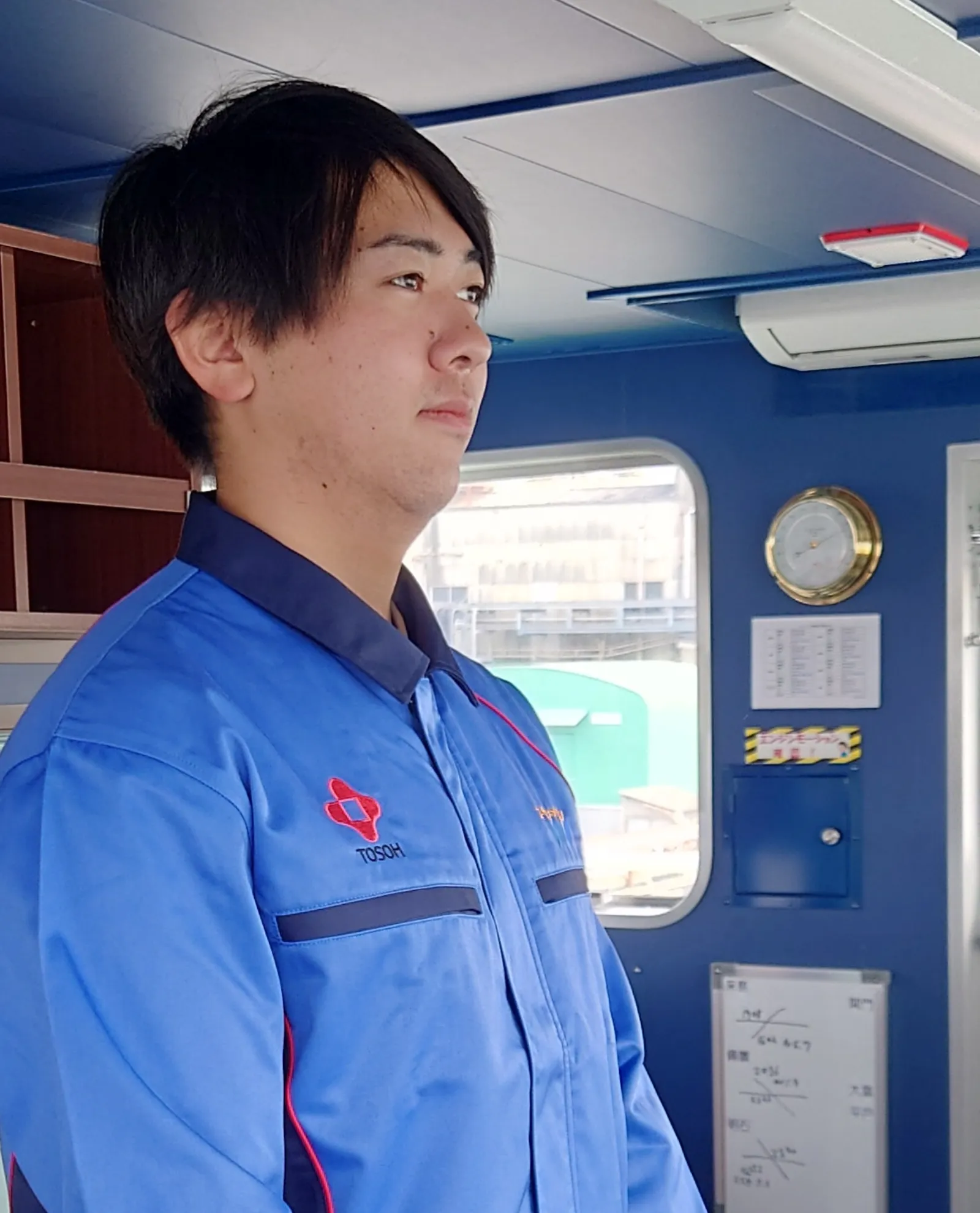 船橋（ブリッジ）で前方を注視する青い作業着の若手船員